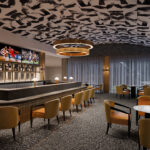 Modern bar interior features sleek decor, sports on televisions, circular chandelier, cozy fireplace, and seating with a monochrome patterned ceiling design.