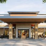 Modern building entrance with a flat roof and stone pillars. People are walking and gathering outside. Trees frame the scene.