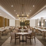 Elegant restaurant interior with modern chandeliers, wooden furniture, and cream decor. Tables are set with floral arrangements, creating a sophisticated atmosphere.